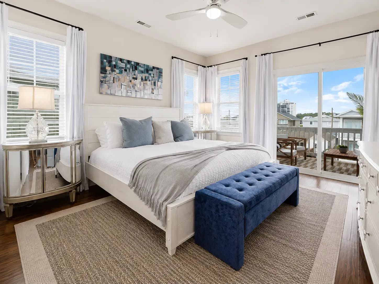 The same bedroom professionally staged by Sojourn — a dressed king bed, art, lamps, rug and a bench